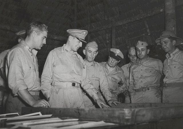 man in military uniform looks at maps with soldiers