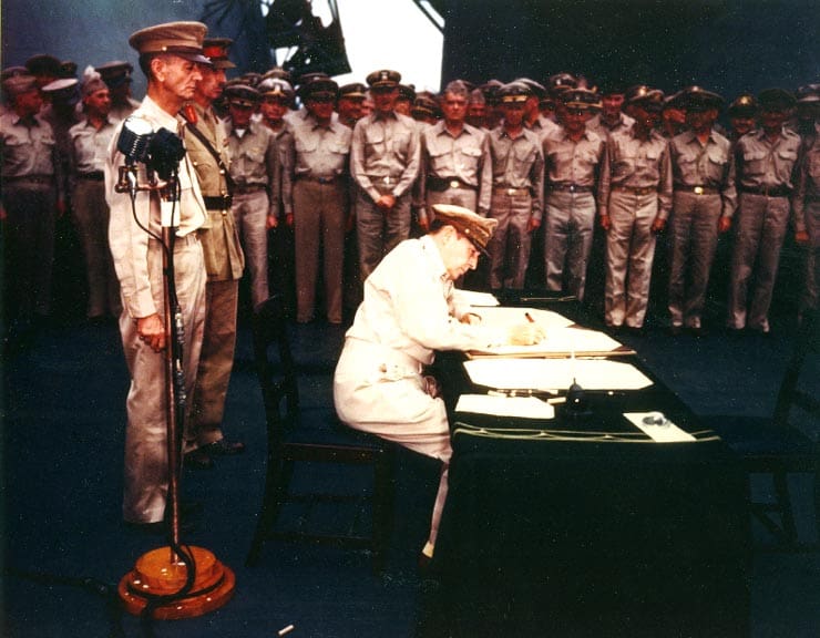 man in military uniform signs document in front of soldiers