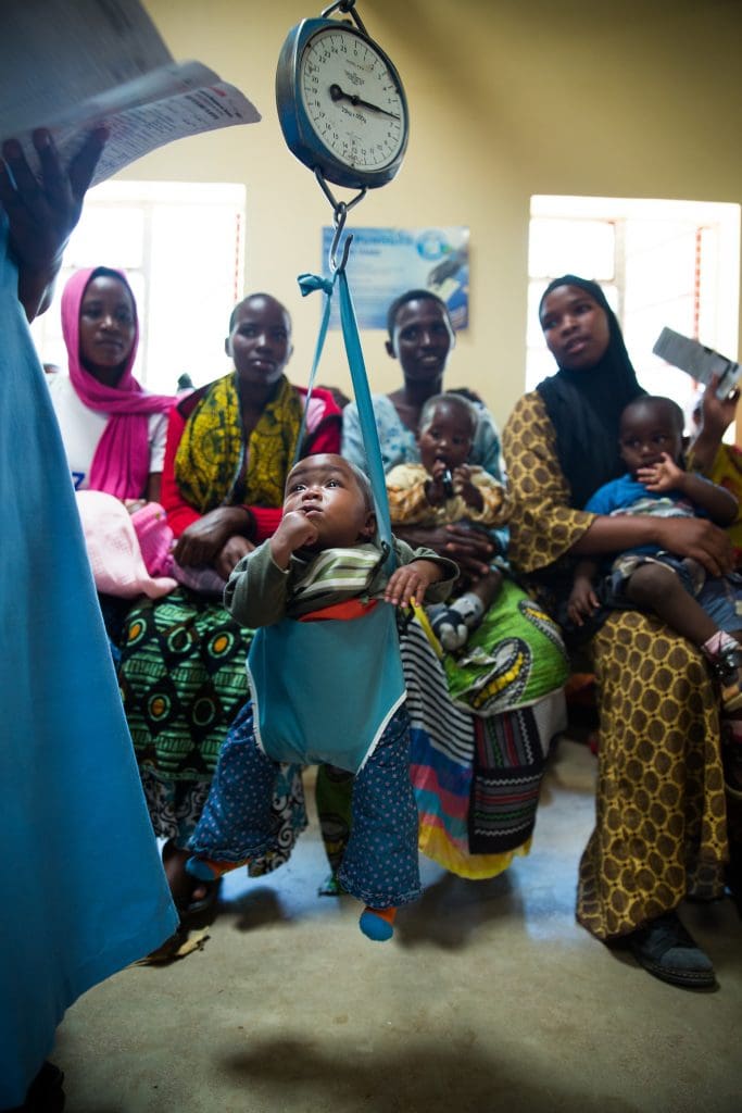 A baby is weighed in a hanging scale at the Makiungu Hospital with mothers from the community watching