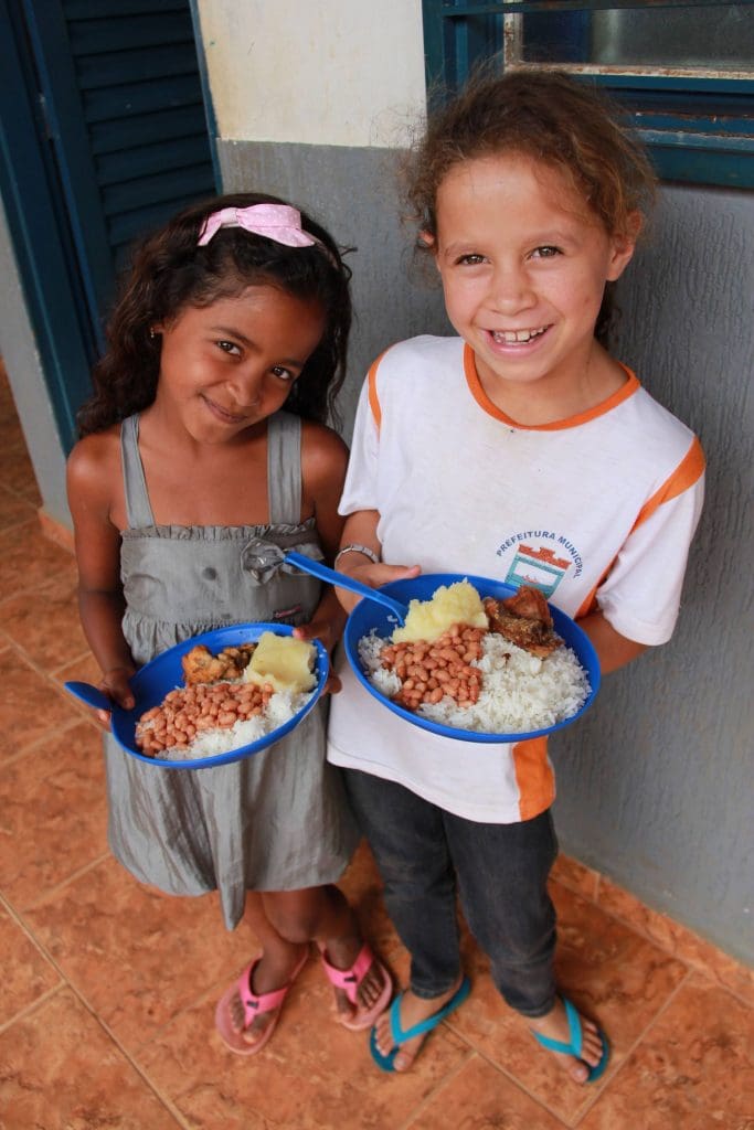 Students in Brazil hold up plates full of rice, beans and cassava from WFP.