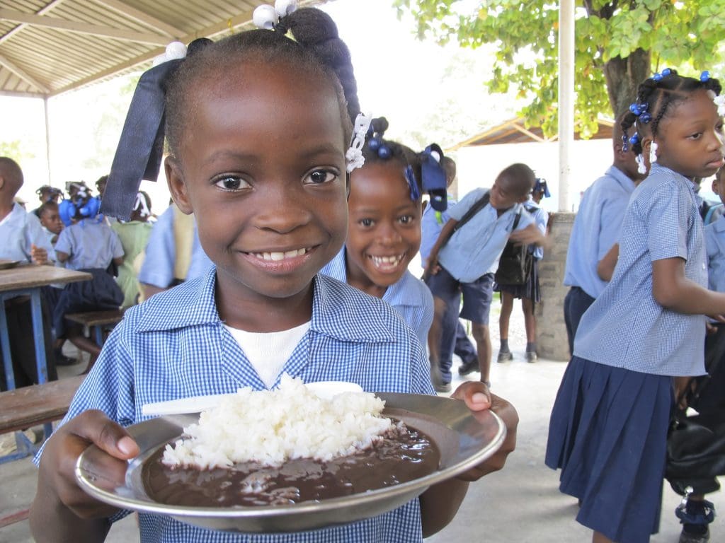 A young girl shows holds up her plate of rice and beans