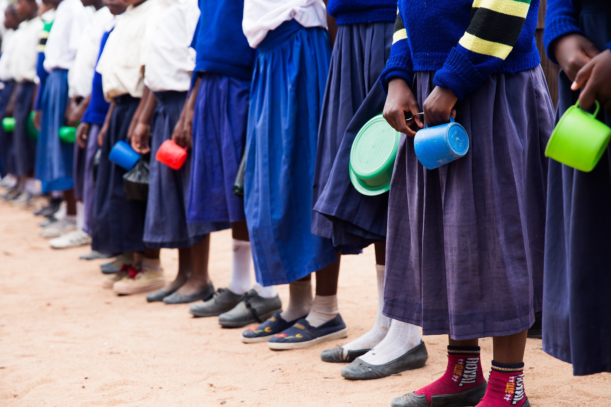 Students lined up, seen from the waist down, holding bowls and cups in their hands