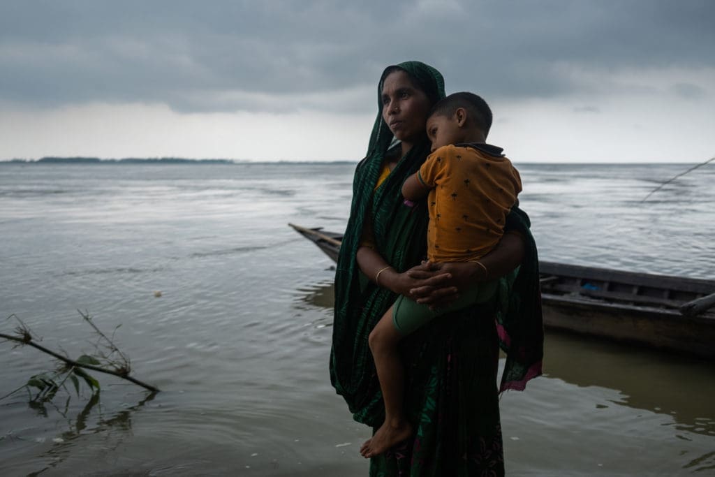 A woman stands in knee-deep water holding her child