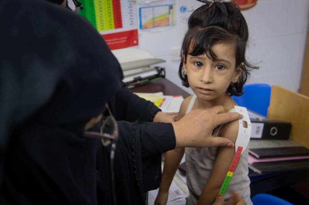 a young girl has her arm measured at a health center in yemen
