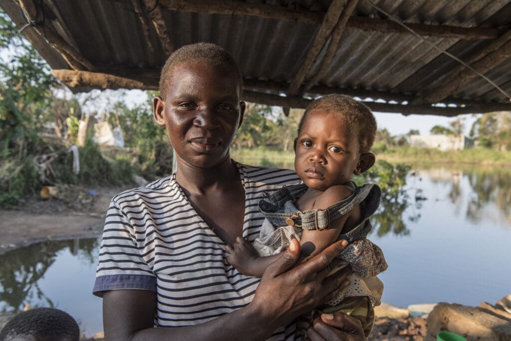 A mother and her baby stand in front of floodwaters in Mozambique