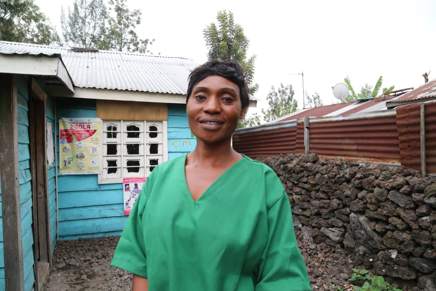 A nurse in green scrubs is pictured standing outside her house, smiling