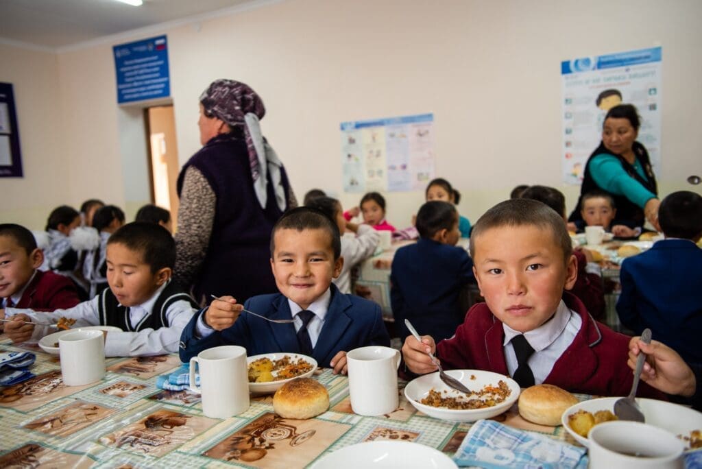 Boys in school uniforms eat their school meal at a long table