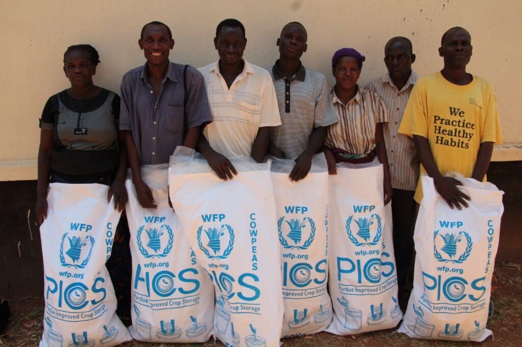 7 people stand in a line holding WFP grain storage bags in front of them