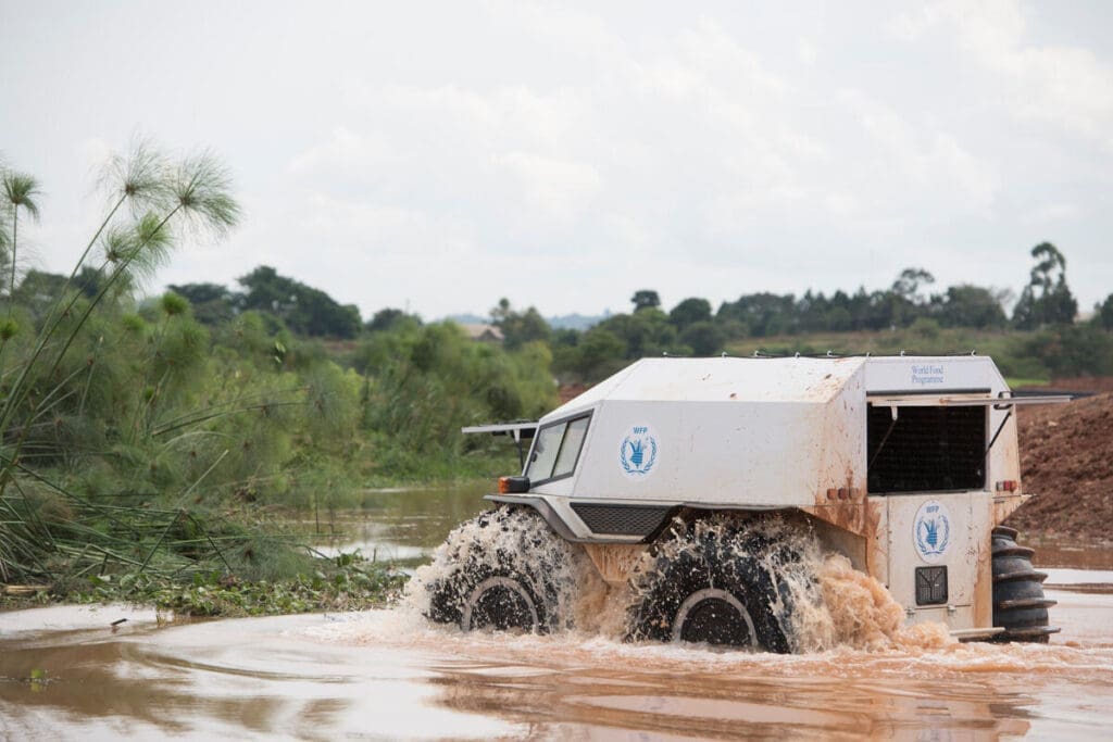 A SHERP vehicle drives across a muddy river.
