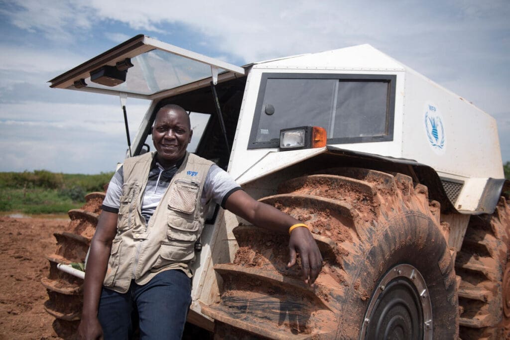 A WFP driver in a vest stands in front of a SHERP vehicle.