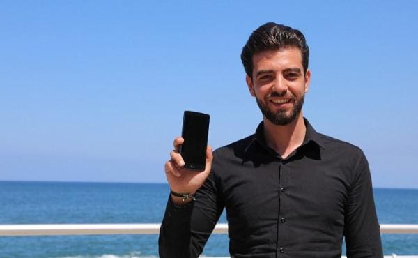 a young man holds up his phone at the beach