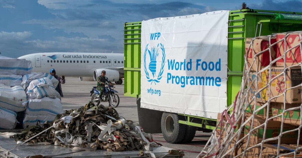 A WFP truck is parked in front of a plane, unloading supplies.