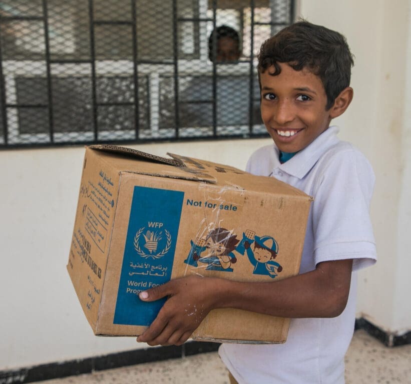A schoolboy holds a box of WFP biscuits, smiling.