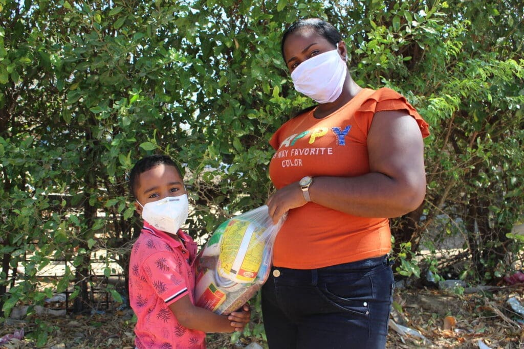 A mother and daughter in masks hold a bag of food.