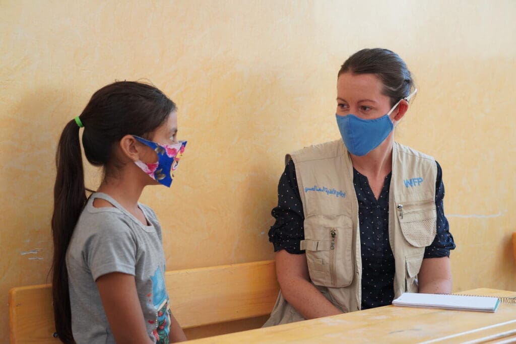 A WFP staff member speaks with a schoolgirl in a mask.