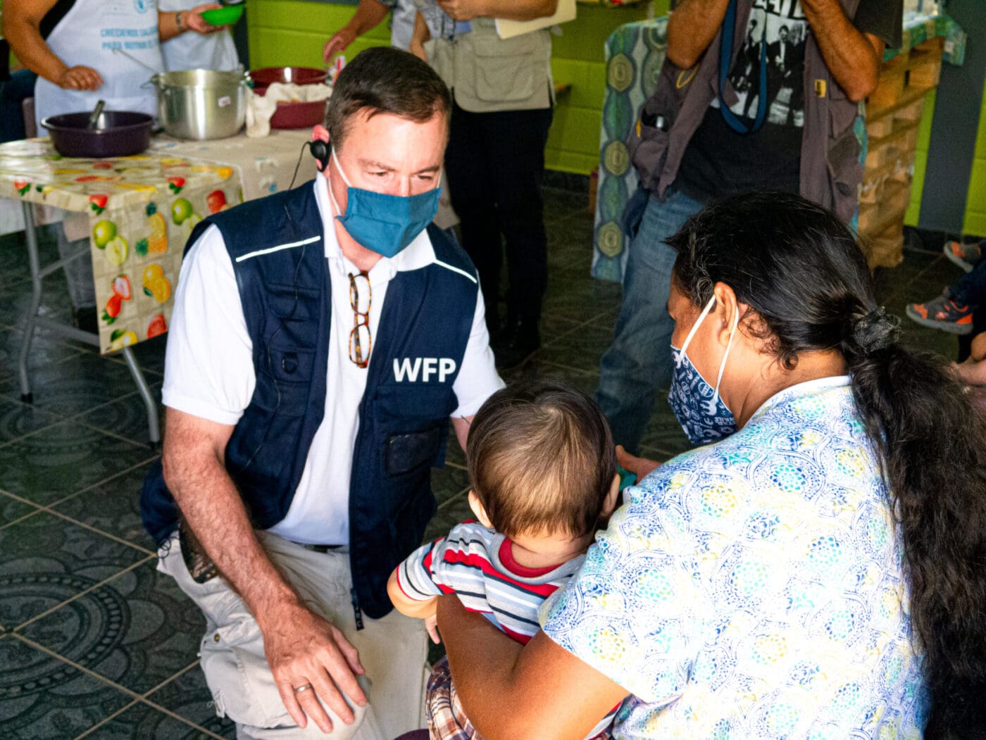 man in WFP vest and covid health mask speaks to mother and child