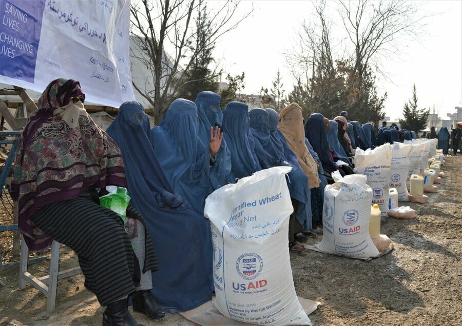 women in burqas sitting next to bags of food