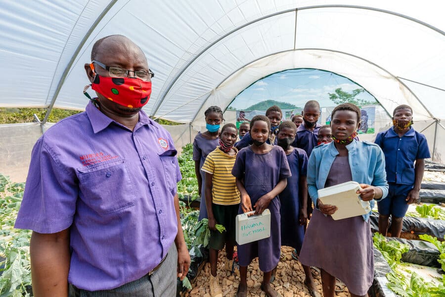 teacher in COVID face mask stands with students in greenhouse