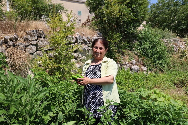 woman stands in garden holding vegetable and smiling