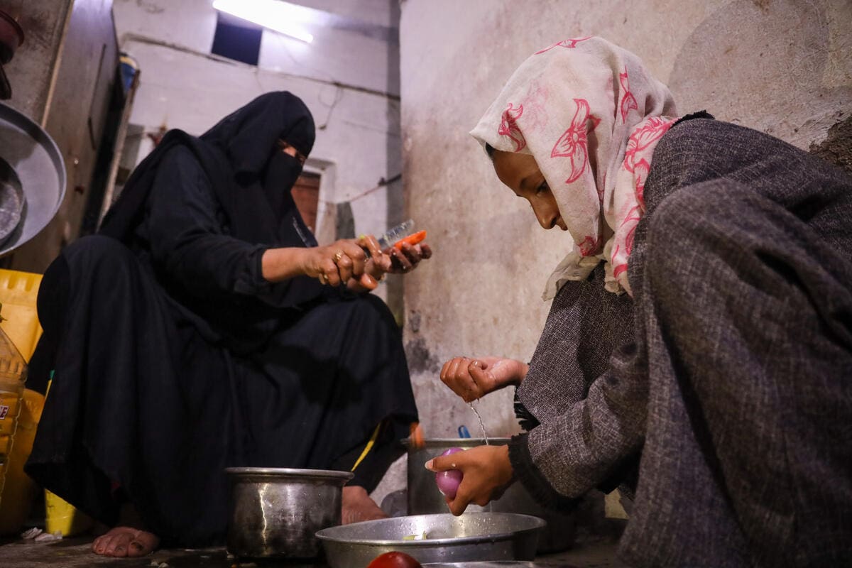 woman in full black burqa cooking in kitchen with granddaughter