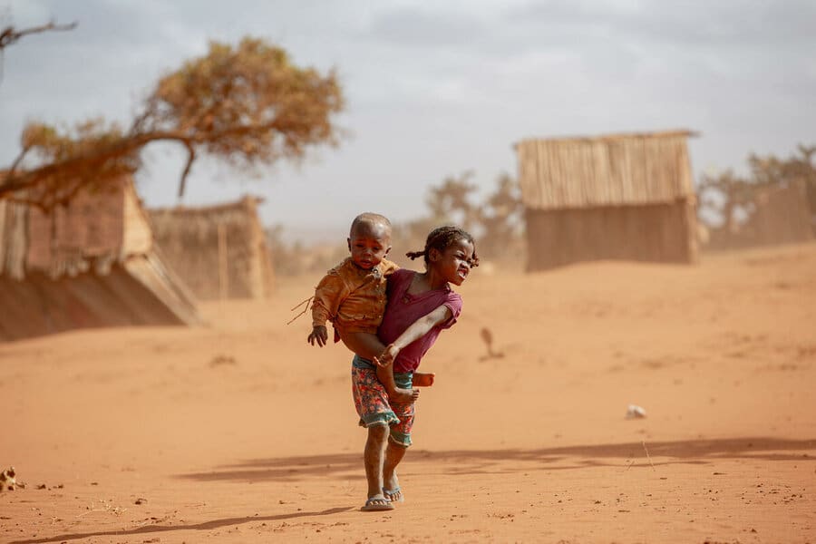 little girl carrying little boy across dusty land