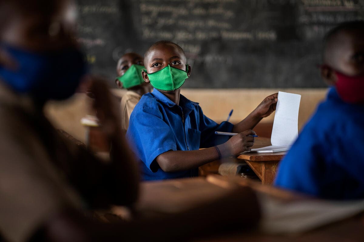 boy in blue uniform and green COVID health mask in classroom