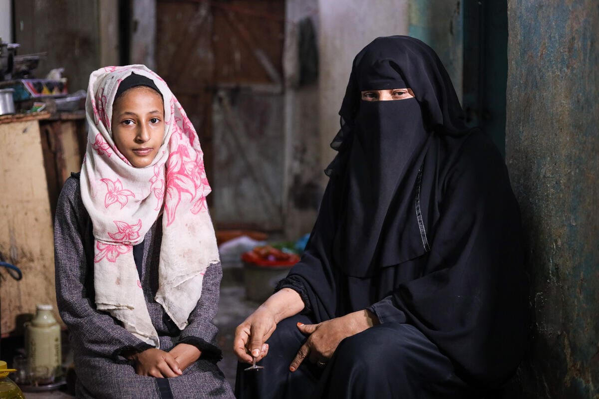 young girl in pink headscarf next to grandmother in black burqa