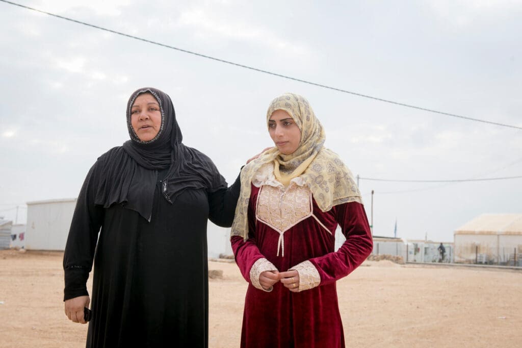 mother in black headscarf and clothes standing with daughter in red and white clothes