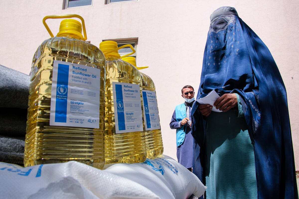 woman in blue burqa picking up sunflower oil