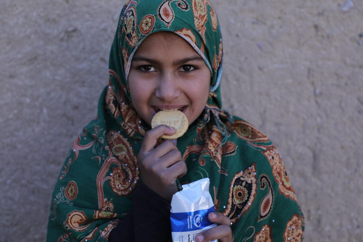 girl in green headscarf eating biscuit and smiling